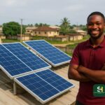 Nigerian man smiling beside rooftop solar panels in a residential area.